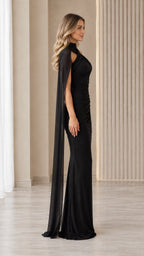 Side profile view of model wearing black ruched evening gown with flowing cape drape