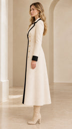 Side profile view of cream double-breasted maxi coat with black trim and tall beige boots