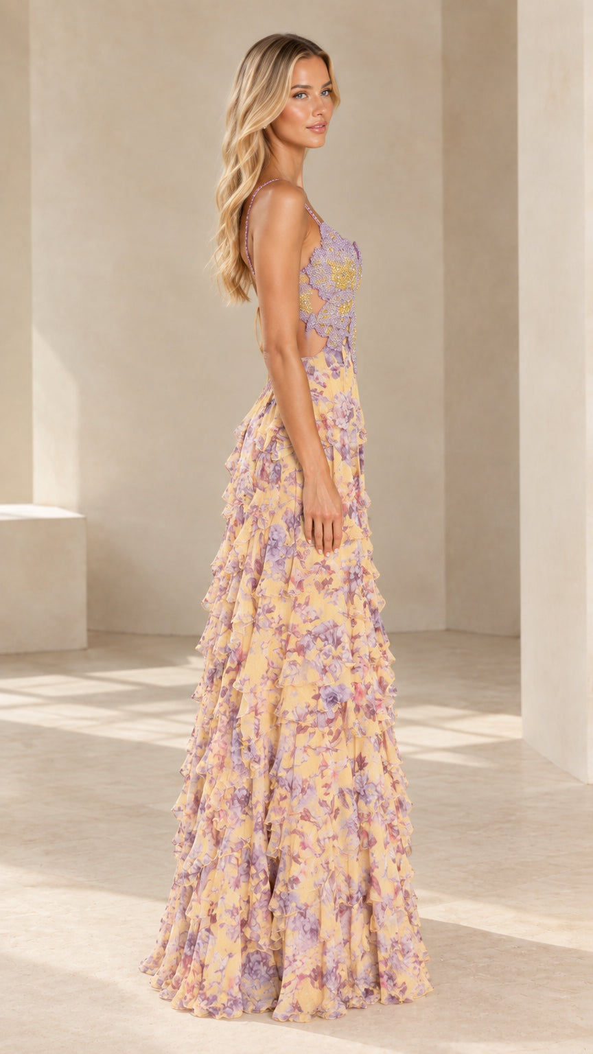 Side angle view of model in yellow floral ruffle maxi evening dress with side waist cutout