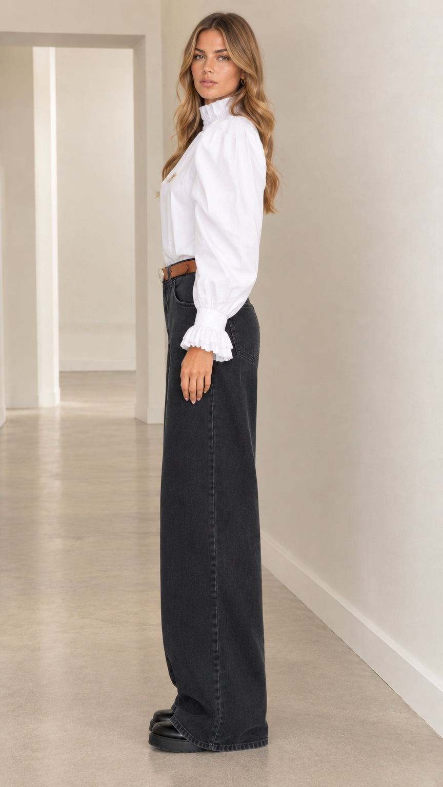 Side profile of woman wearing white ruffle collar puff-sleeve top and charcoal wide-leg denim trousers