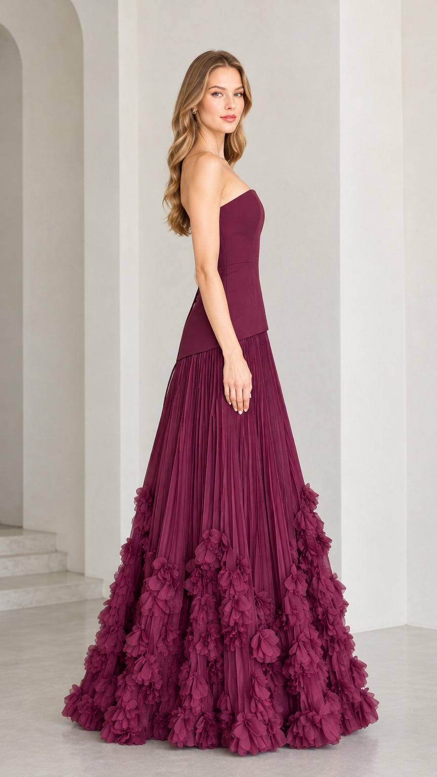 Side profile of strapless burgundy pleated formal gown with floral appliqué detailing