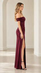 Side full-length view of woman wearing burgundy satin off-the-shoulder evening gown with slit