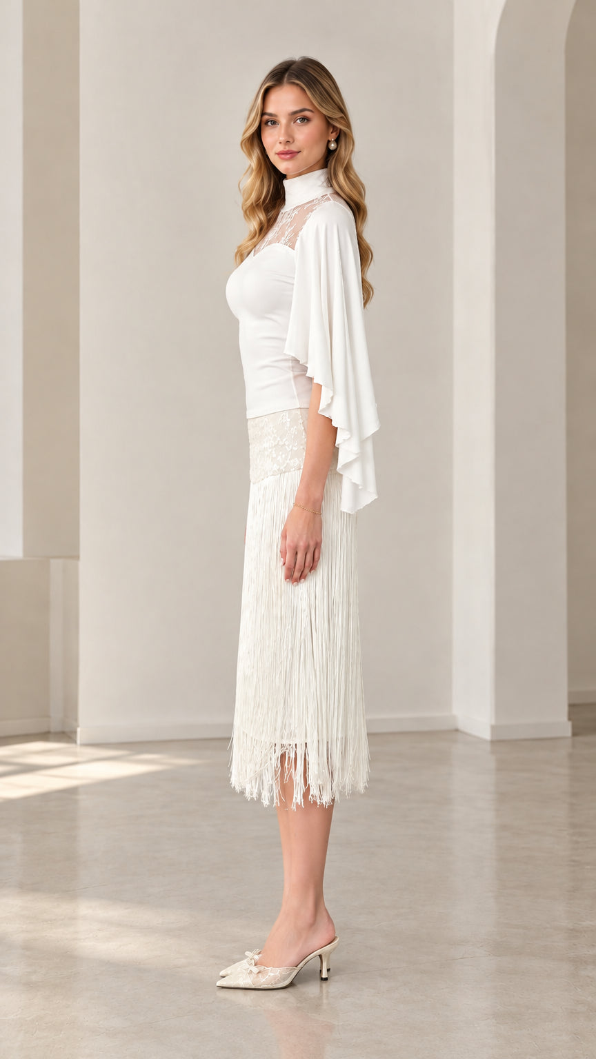 Side profile of model in white high-neck capelet top and tassel fringe skirt