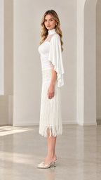 Side profile of model in white high-neck capelet top and tassel fringe skirt