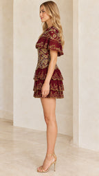 Side view of woman posing in burgundy capelet mini dress with tiered skirt