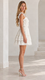 Side profile view of model wearing white tiered lace mini dress with ruffle straps