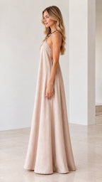 Side profile of model wearing flowy beige sleeveless halter maxi dress