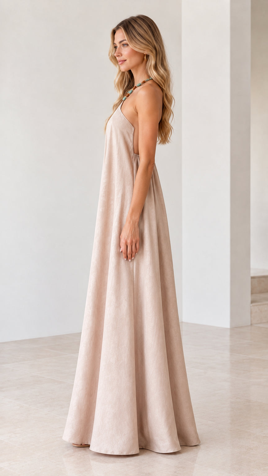 Side profile of model wearing flowy beige sleeveless halter maxi dress