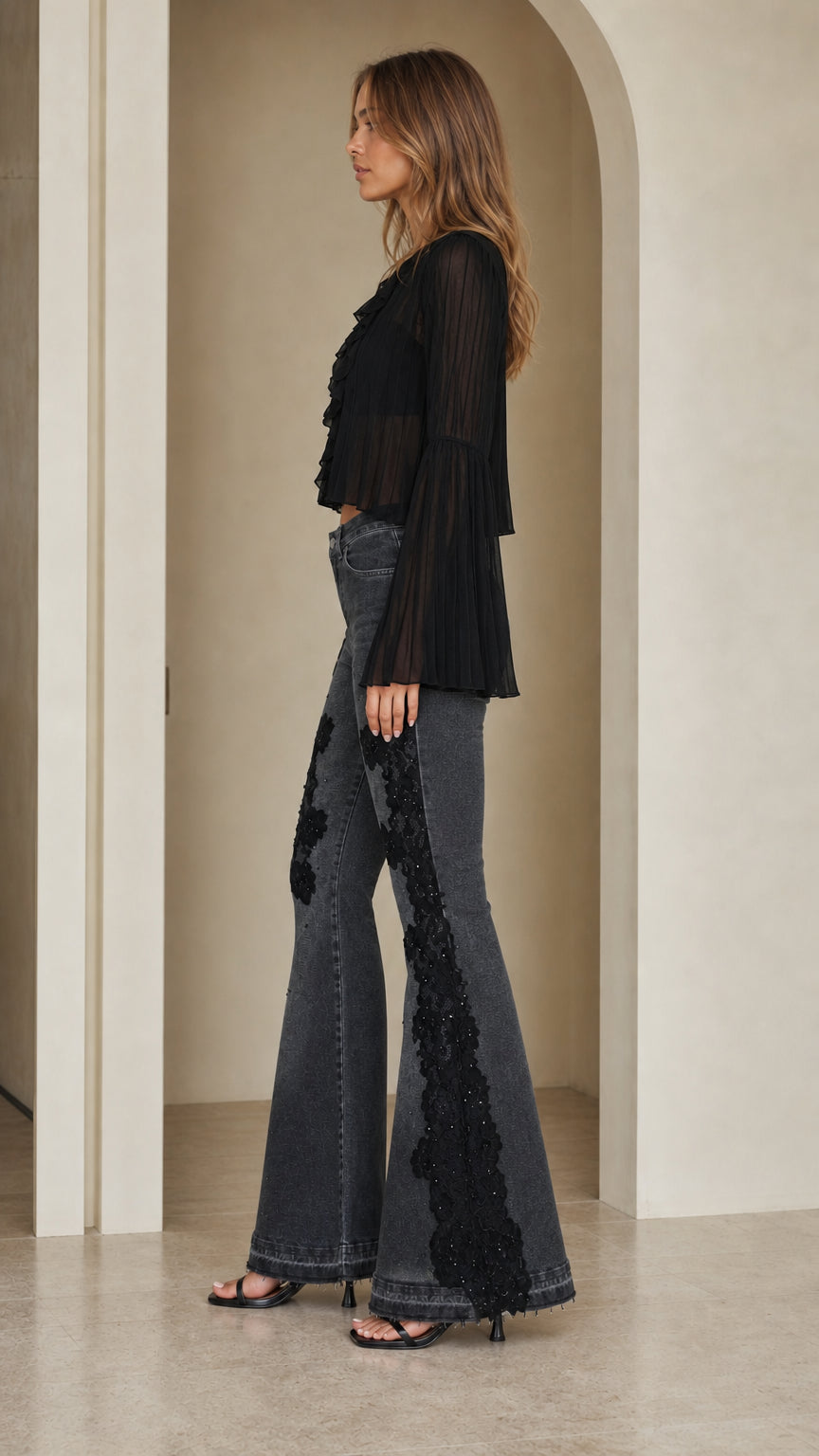 Side profile view showing dramatic flare and lace appliqué on washed black jeans