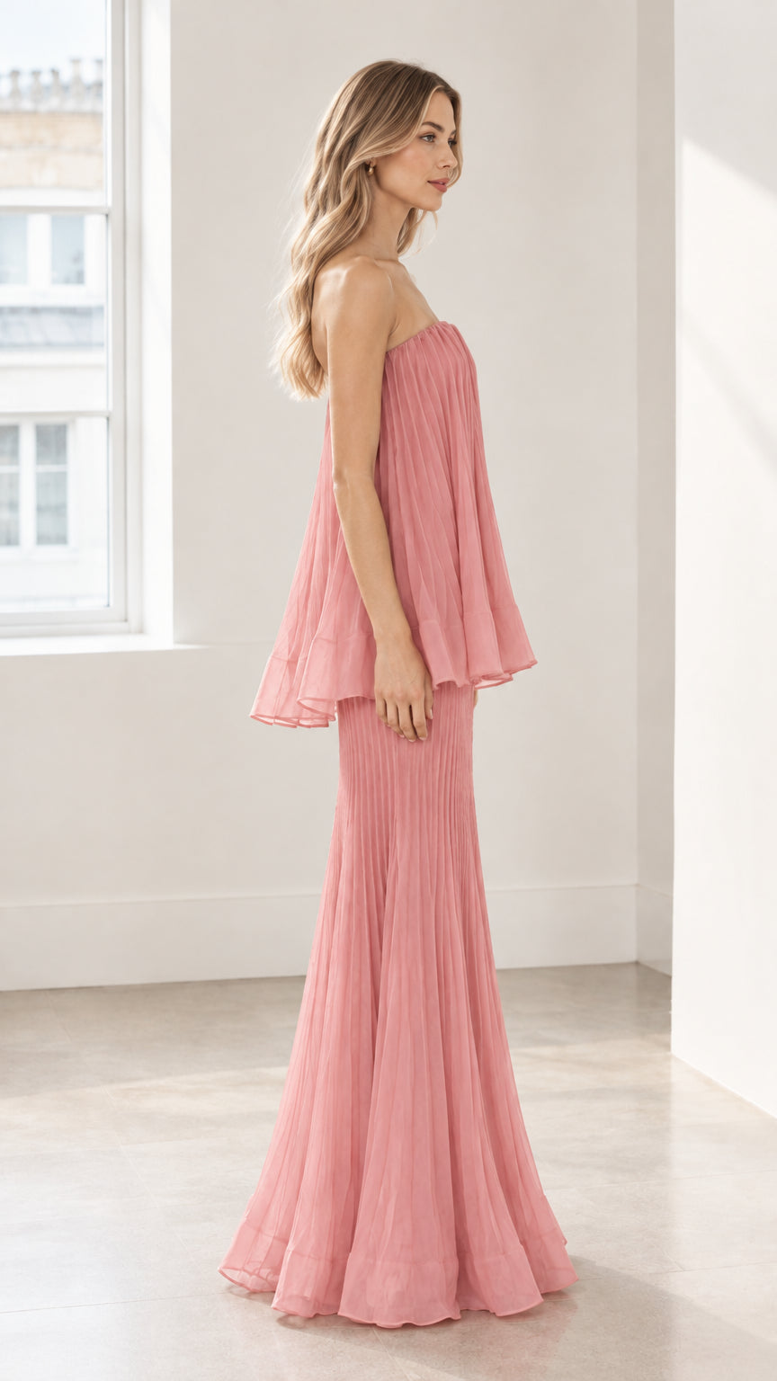 Side full-length view of dusty pink strapless pleated maxi gown showcasing draped tier silhouette