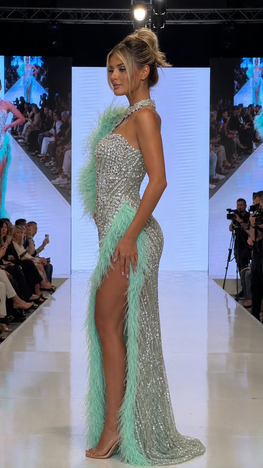 Side profile of silver crystal embellished formal gown showing high leg slit and feather detailing