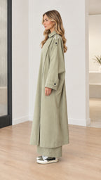 Side profile view of model in floor-length sage green duster trench coat