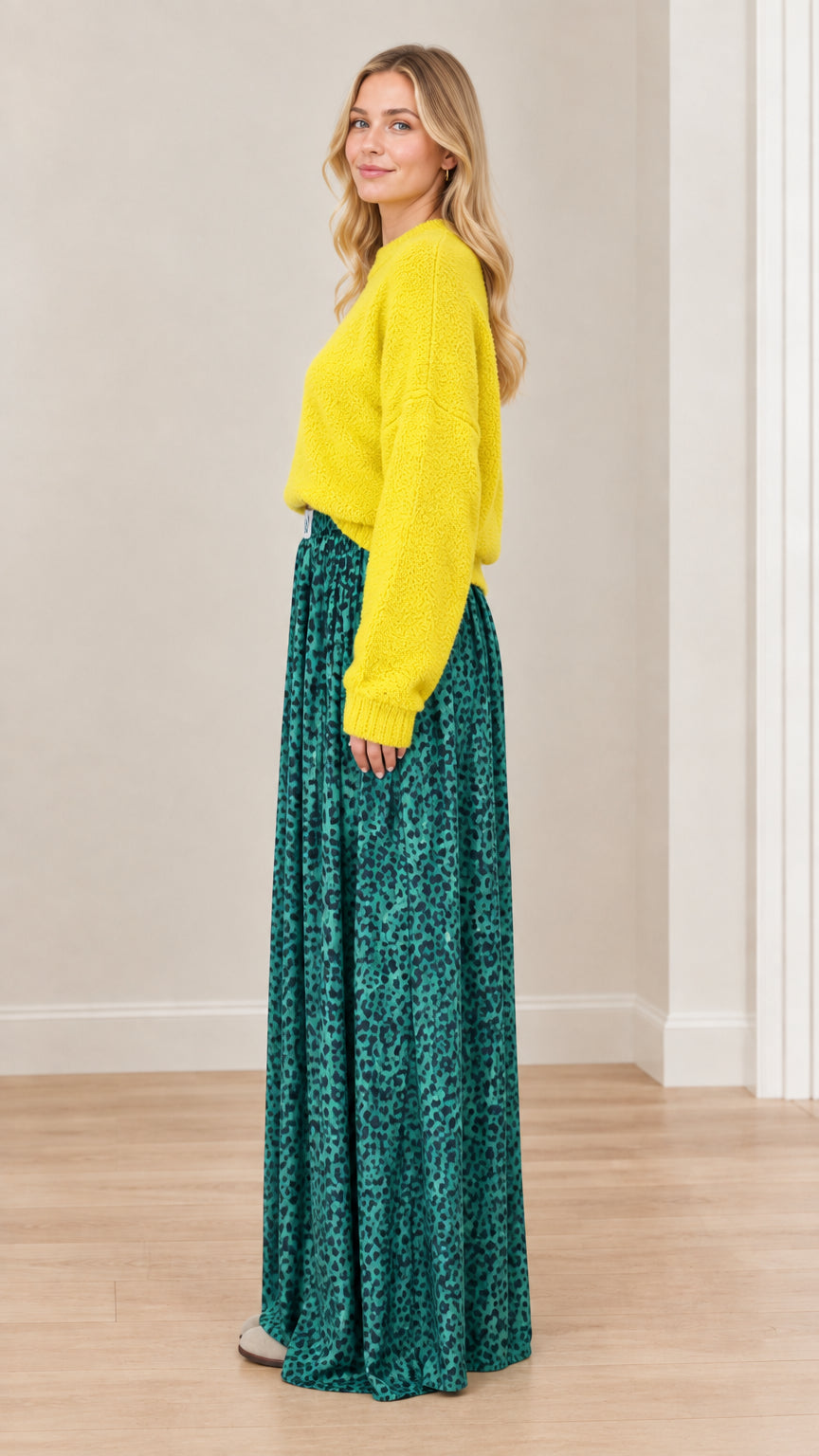 Side angle view of model styled in yellow sweater and emerald green animal print wide-leg pants