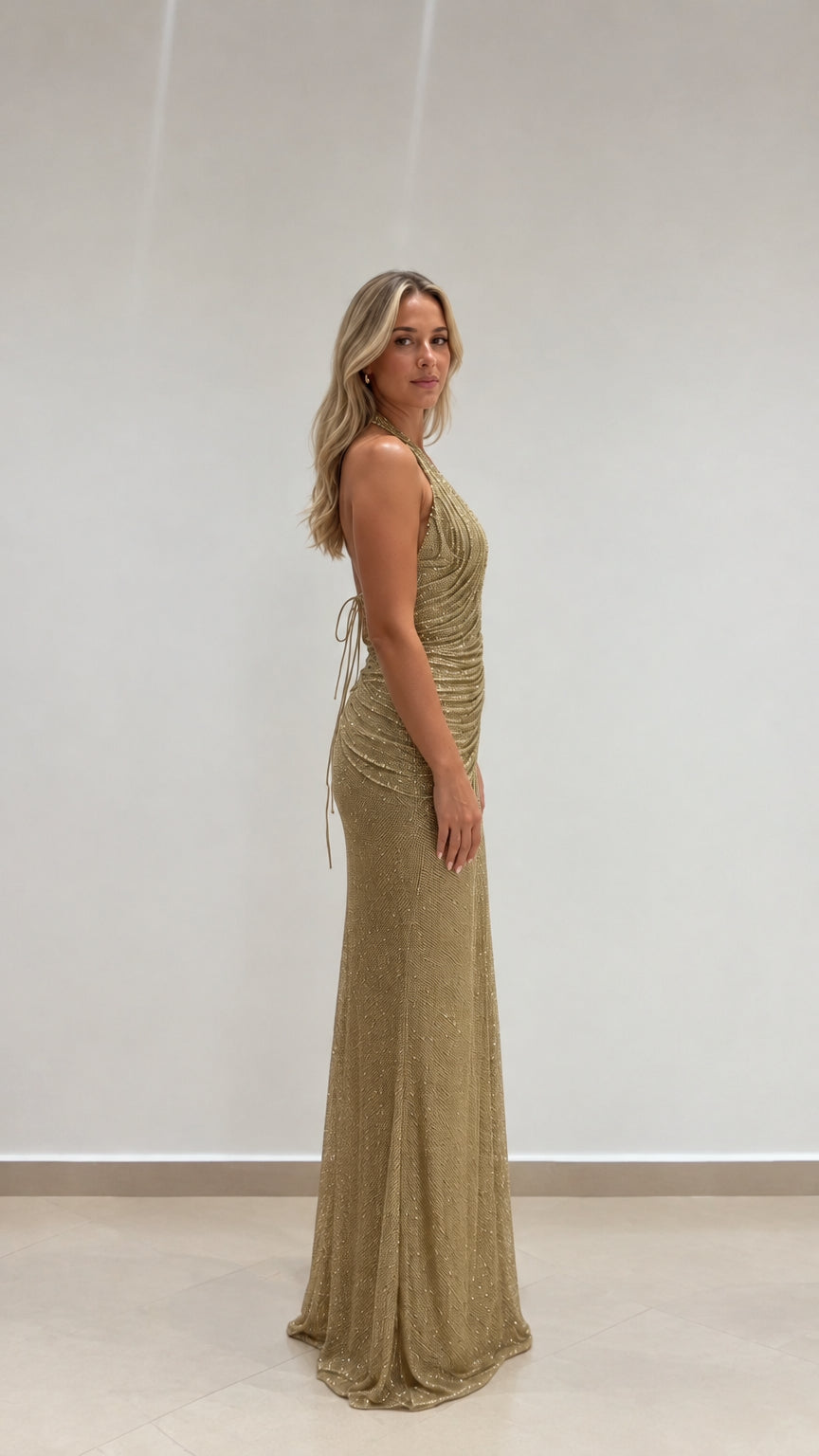 Side profile of model wearing floor-length gold glitter halter maxi dress
