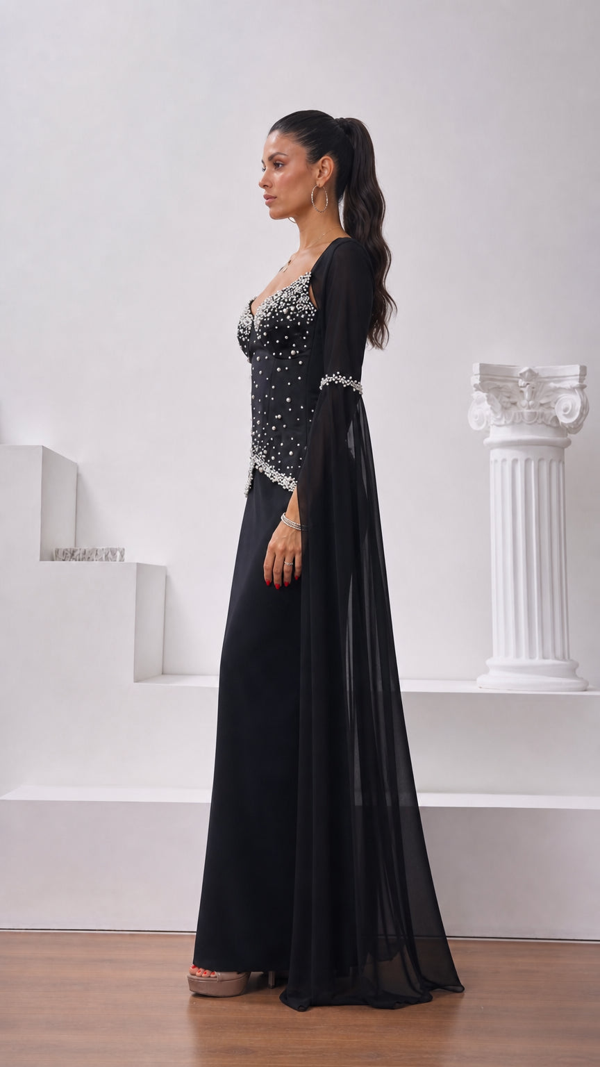 Side profile view of black evening gown showing corset structure and flowing cape sleeve detail