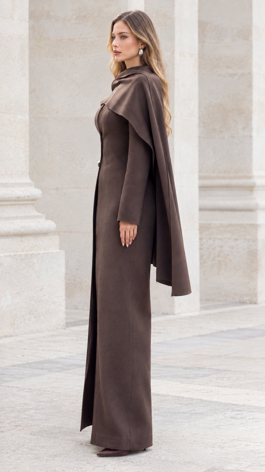 Side profile view of model wearing brown capelet maxi jacket and matching pants