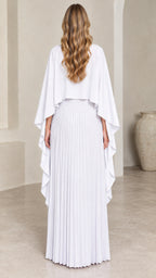 Back view of woman wearing white pleated cape maxi dress with draped overlay
