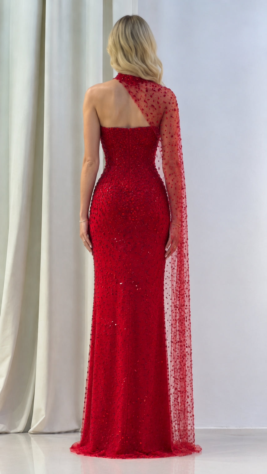 Back view of model showing the back cut and trailing cape of the red evening gown