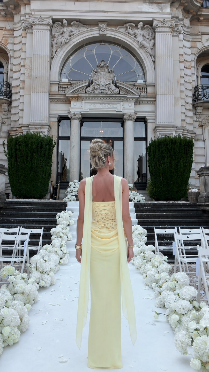 Full back view of woman in pale yellow corset evening dress highlighting the lace-up back and draped waist detail