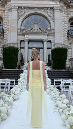 Full back view of woman in pale yellow corset evening dress highlighting the lace-up back and draped waist detail
