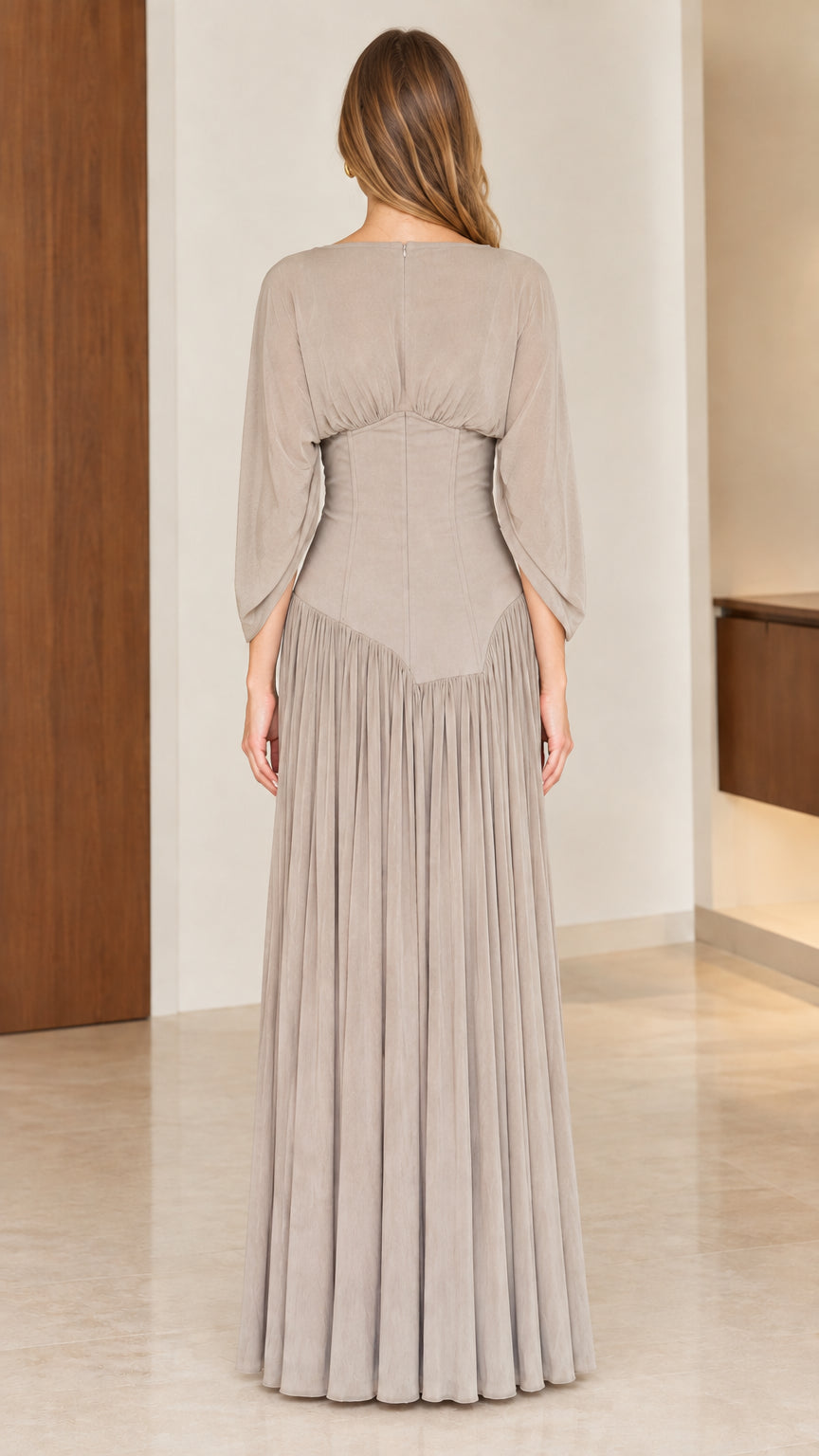 Back full-length view of woman in taupe floor-length dress showing tailored waist and pleats