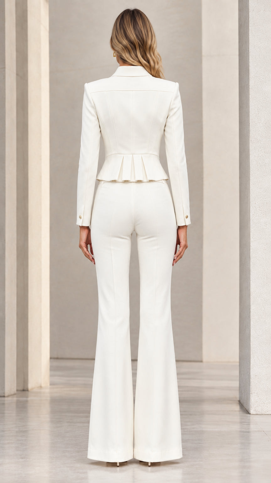 Back view of model wearing white cropped suit jacket with pleated hem and flared trousers