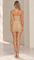 Back view of model in gold sequin ruched mini dress with thin straps