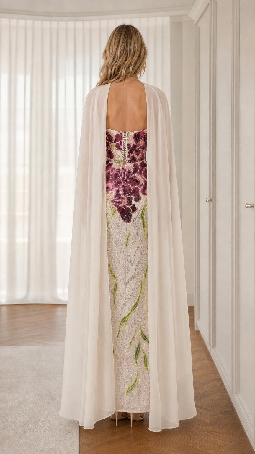 Back view of model wearing white floral sequin maxi gown with sweeping cape
