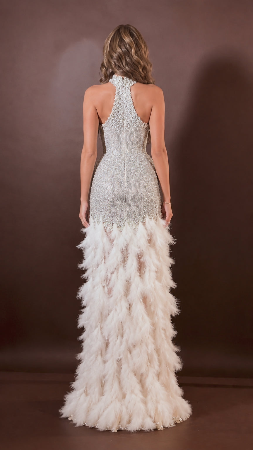Back view of model wearing silver white open-back halter gown with full feather skirt