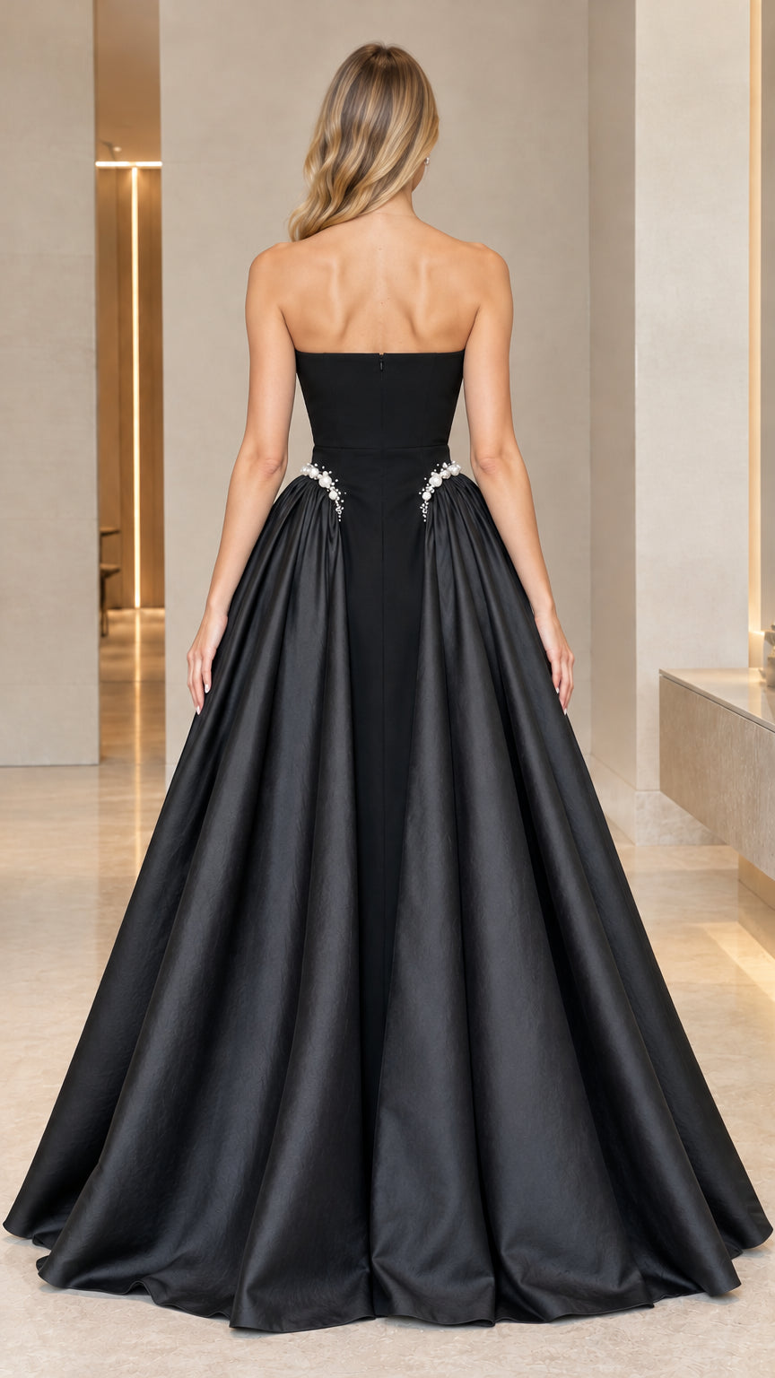 Back full-length view of black strapless formal gown with concealed zipper and gathered overskirt