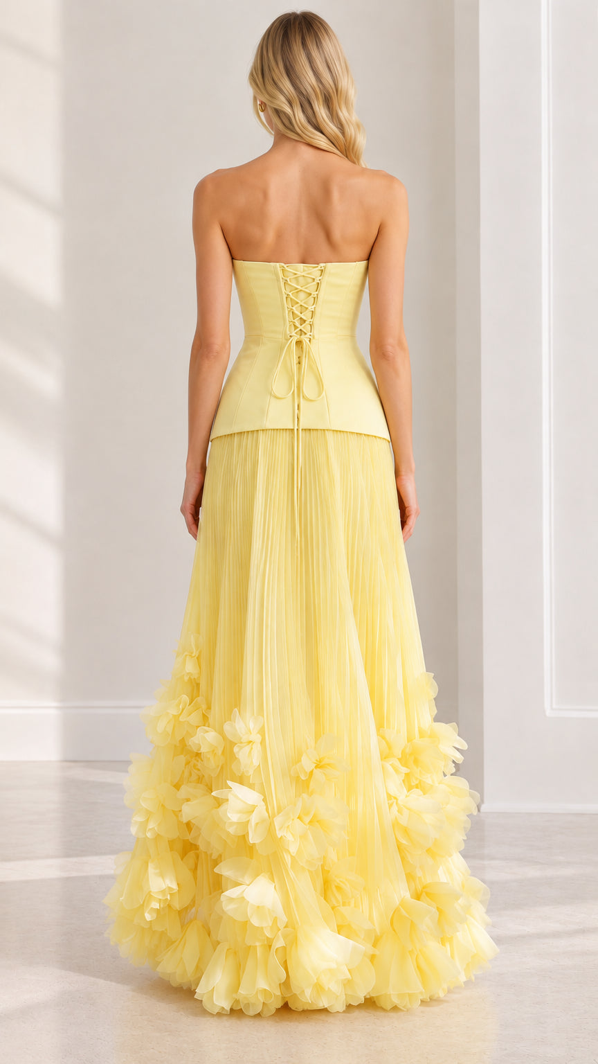 Back view of pastel yellow formal gown featuring lace-up corset detail and floral hem