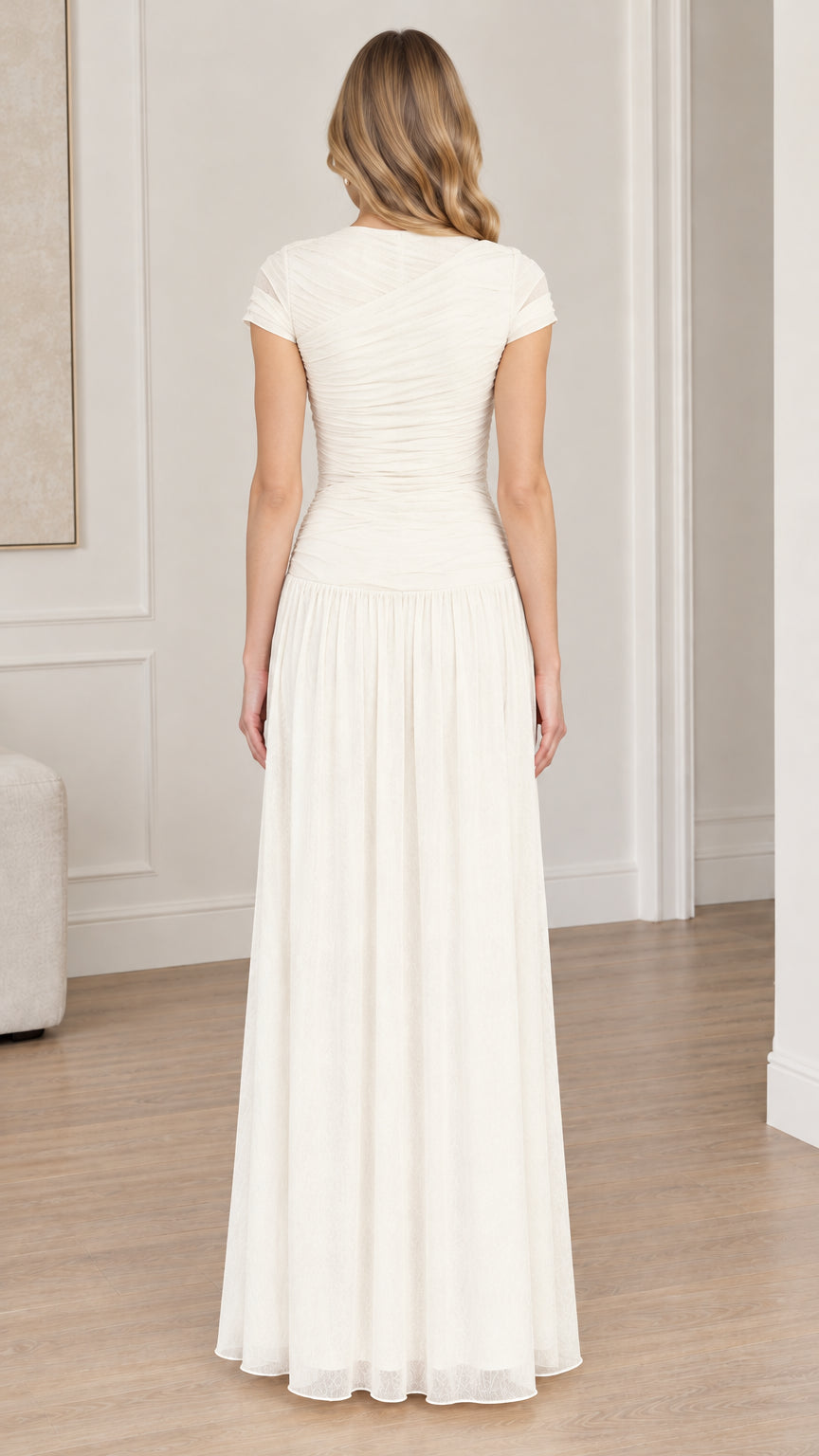 Back full-length view of woman wearing ivory ruched bodice drop-waist maxi dress