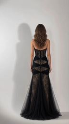 Back full-length view of black strapless evening gown showing boned corset and flared tulle train