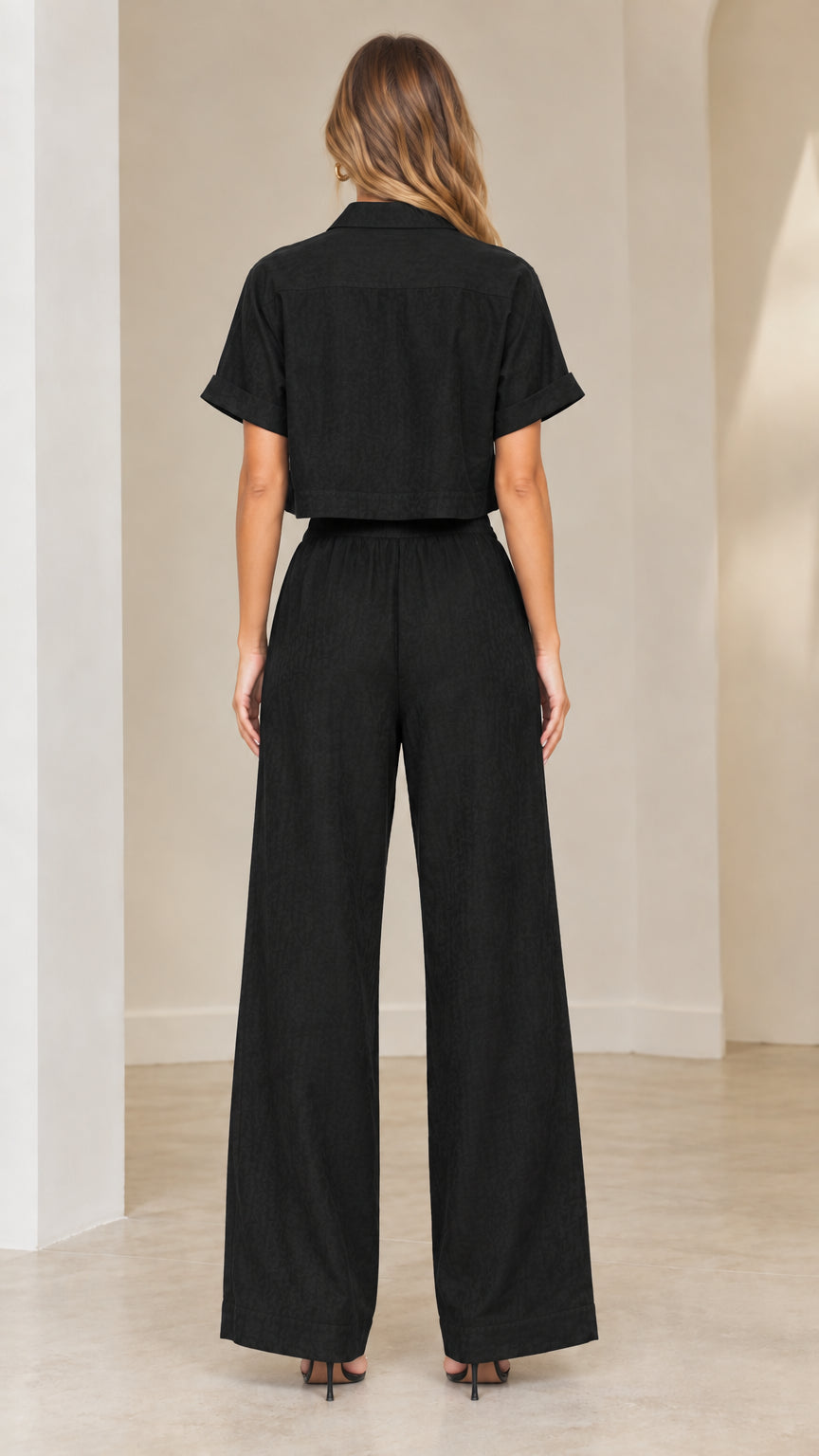 Back view of woman wearing black short-sleeve collared crop shirt and wide-leg pants
