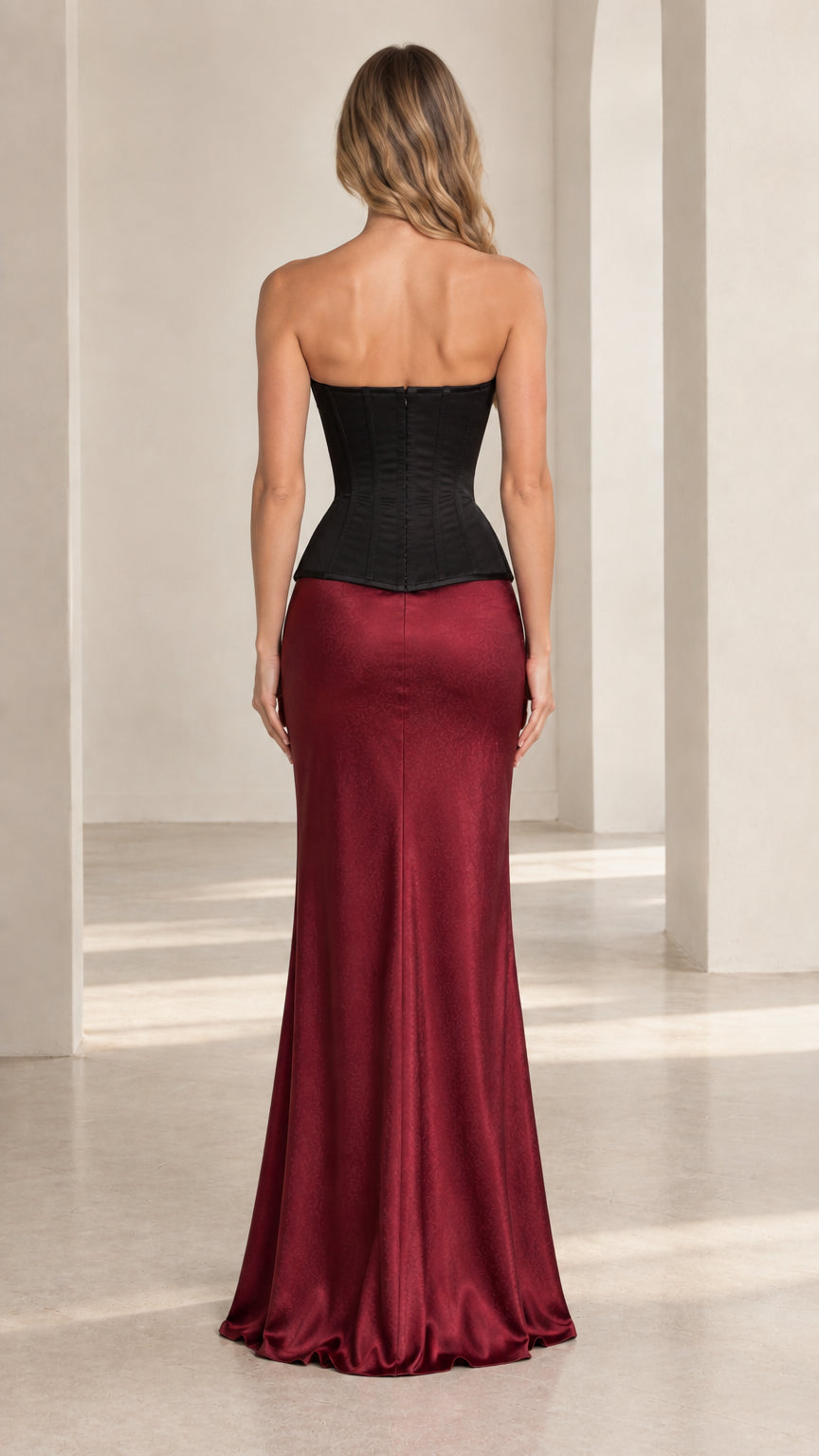 Back view of model showcasing black lace-up corset top and floor-length burgundy skirt