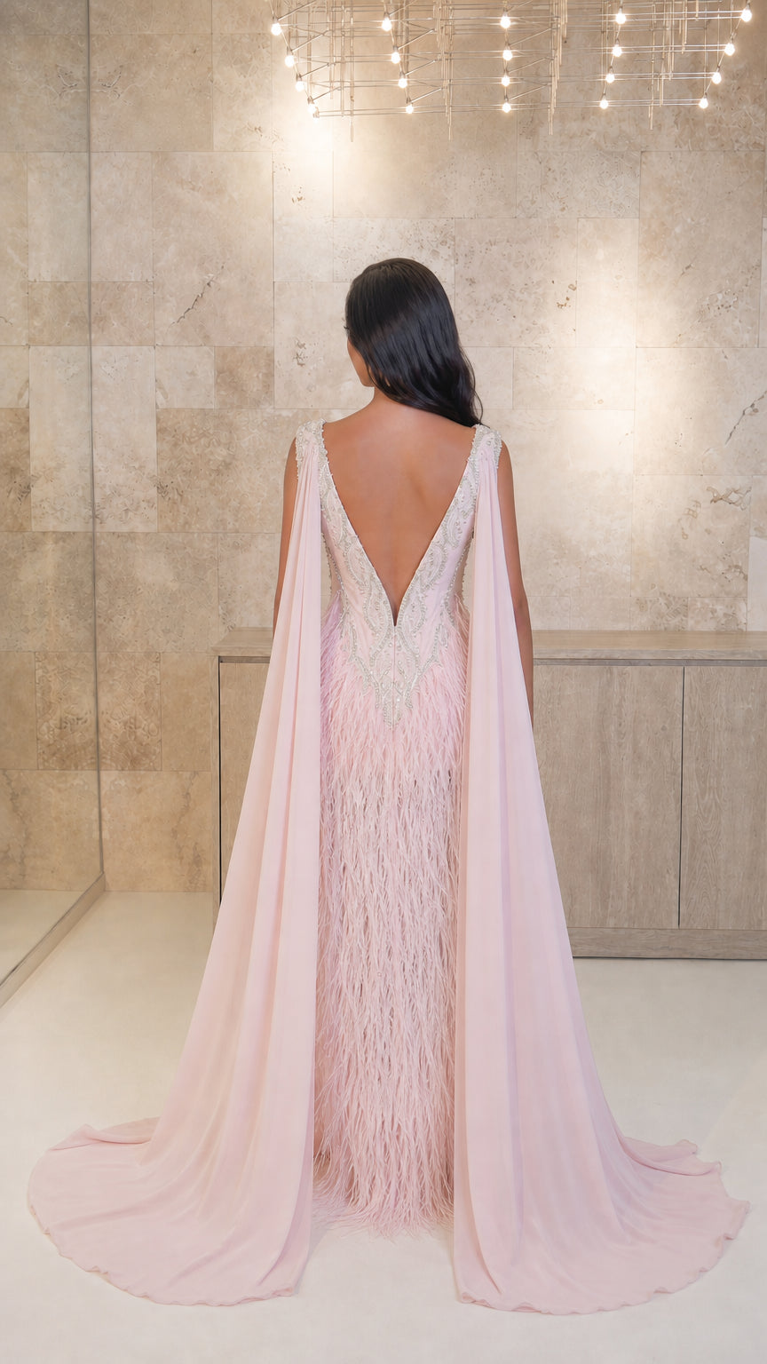 Model wearing Blush Pink evening gown showing open V-back and flowing cape train