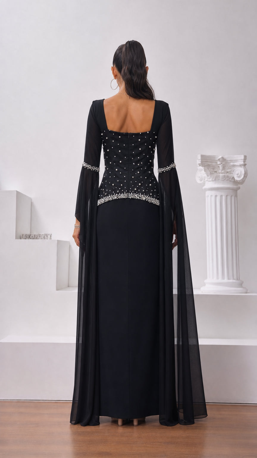 Back view of model wearing black floor-length formal gown with pearl accents and square neckline