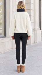 Back view of woman wearing cozy white sherpa fleece jacket paired with black leggings and boots