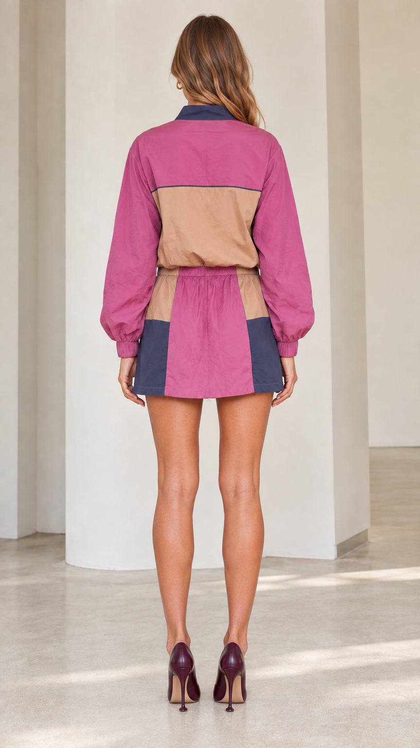 Back full view of woman wearing magenta colorblock long sleeve pullover and mini skirt