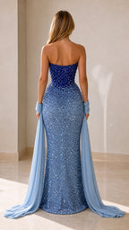 Back view of a royal blue strapless sequin mermaid gown with trailing pale blue drapes