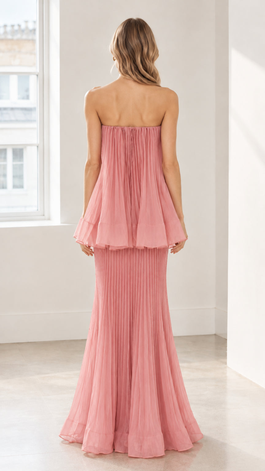 Back full-length view of model in dusty pink strapless pleated evening gown