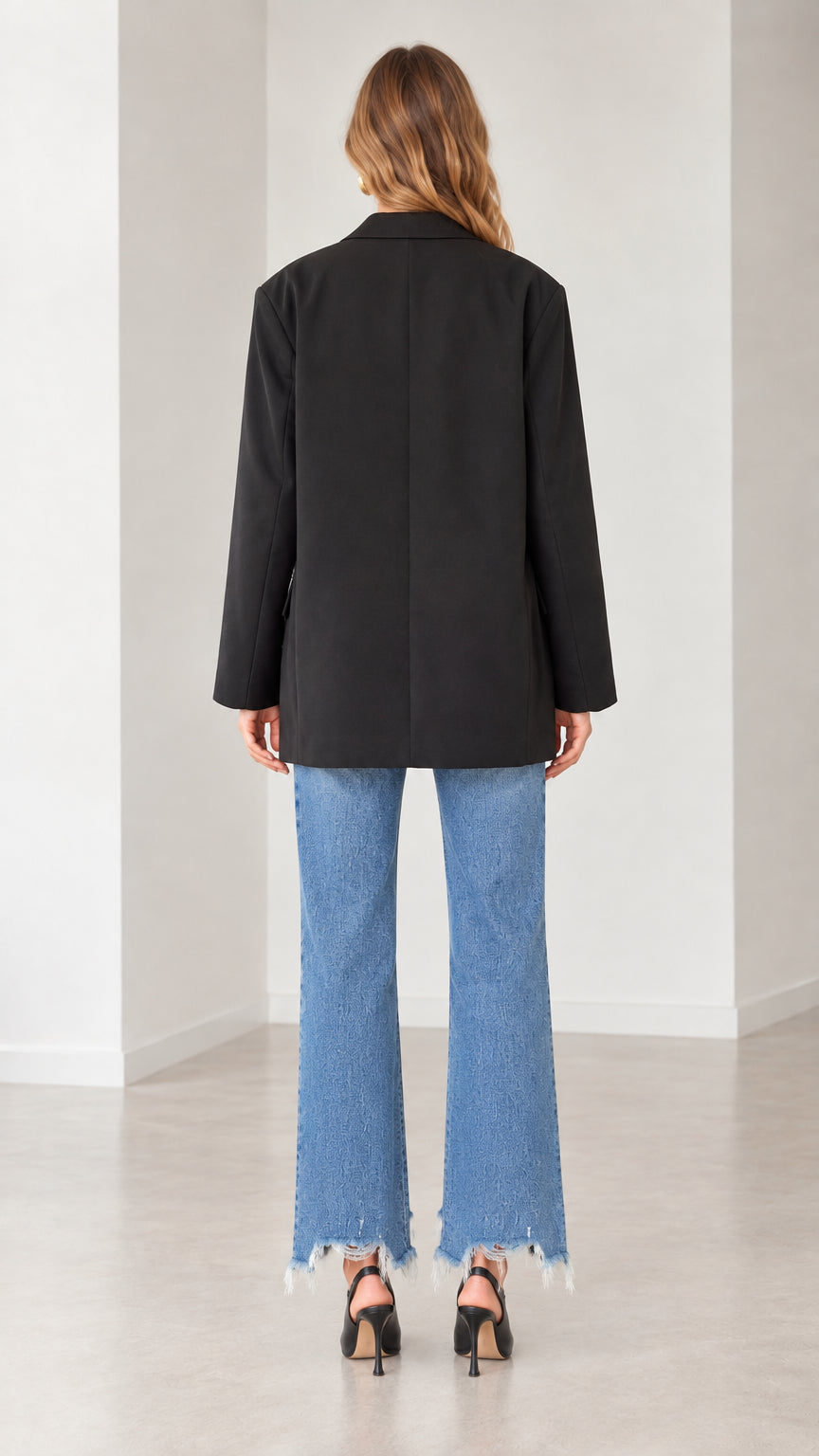 Back view of a model in an oversized black blazer paired with straight-leg denim