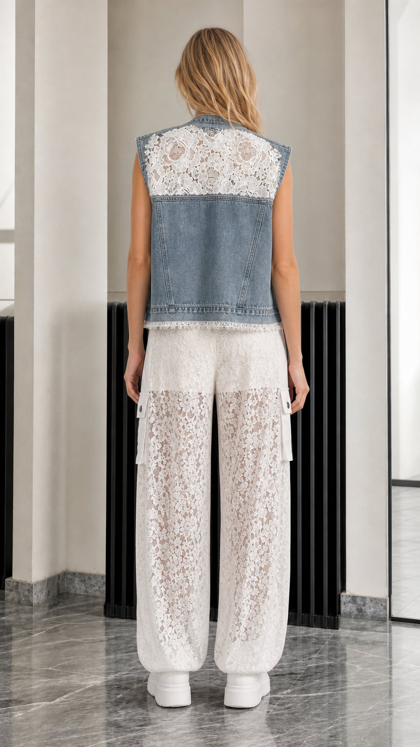 Back view of model wearing denim vest with lace back panel and white lace trousers