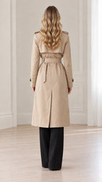 Rear view of women's beige long trench coat highlighting back storm flap and belted waist