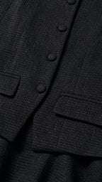 Close up detail of black tweed woven fabric with covered buttons and flap pockets