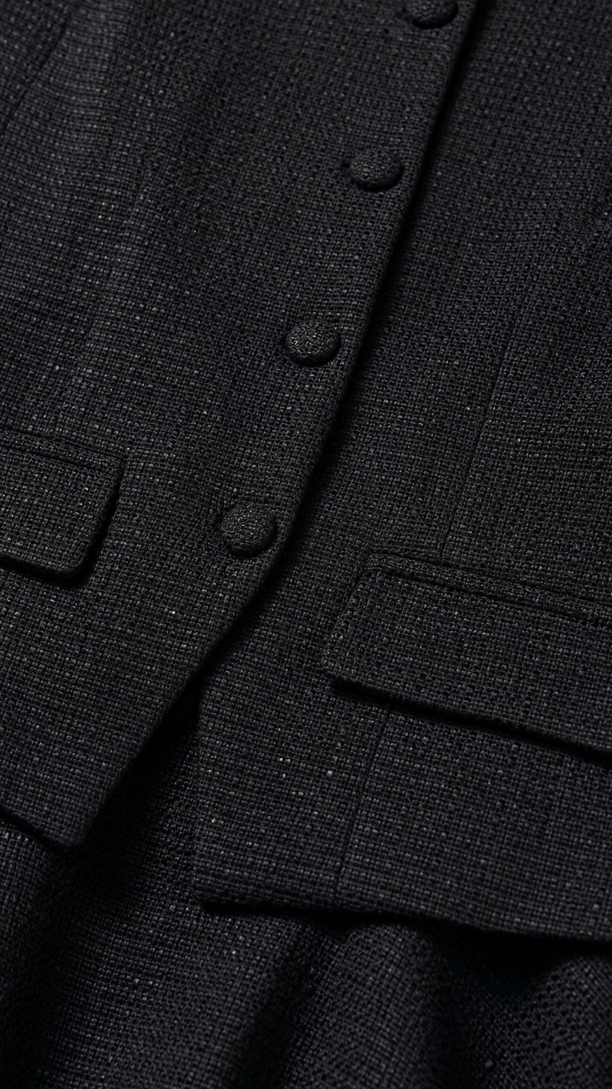 Close up detail of black tweed woven fabric with covered buttons and flap pockets