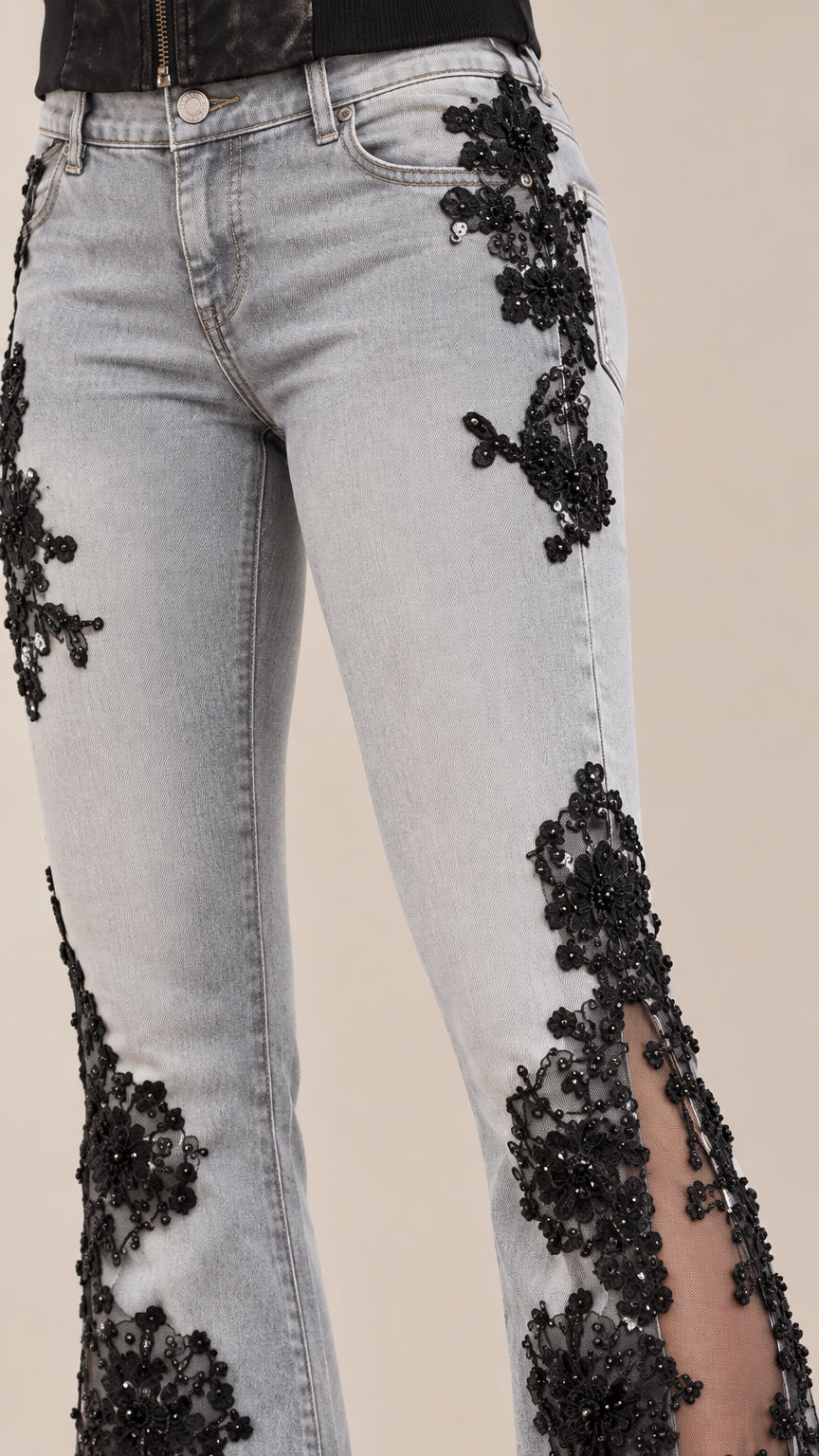 Close-up detail of embroidered floral lace applique on waistband and thigh of light blue denim