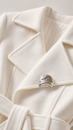 Close-up detail of white wool-blend coat collar, lapels, and silver metallic brooch