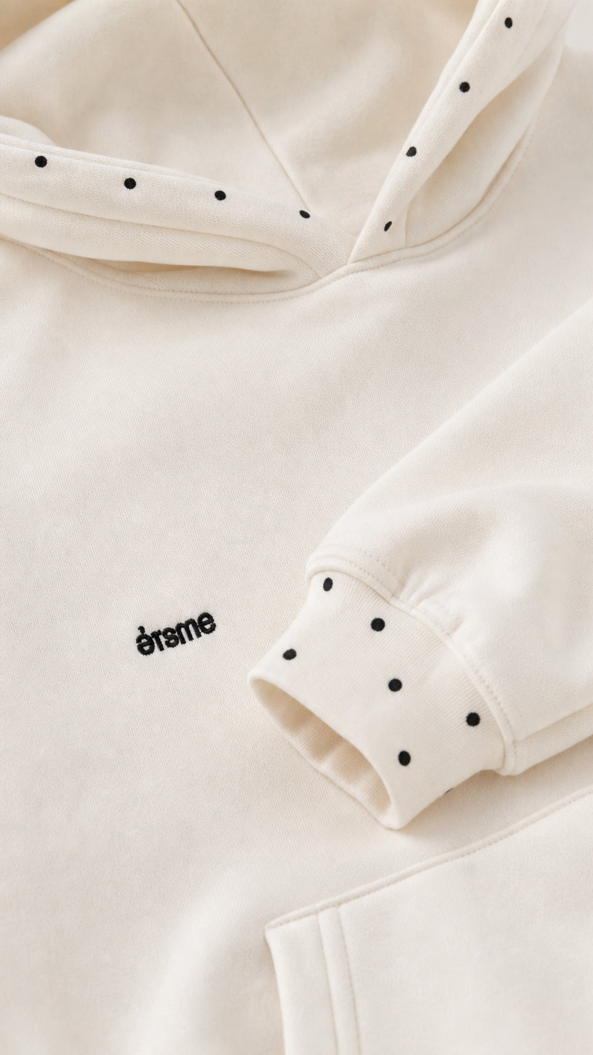 Close-up detail of cream hoodie showing hood micro studs and cuff accent