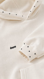Close-up detail of cream hoodie showing hood micro studs and cuff accent